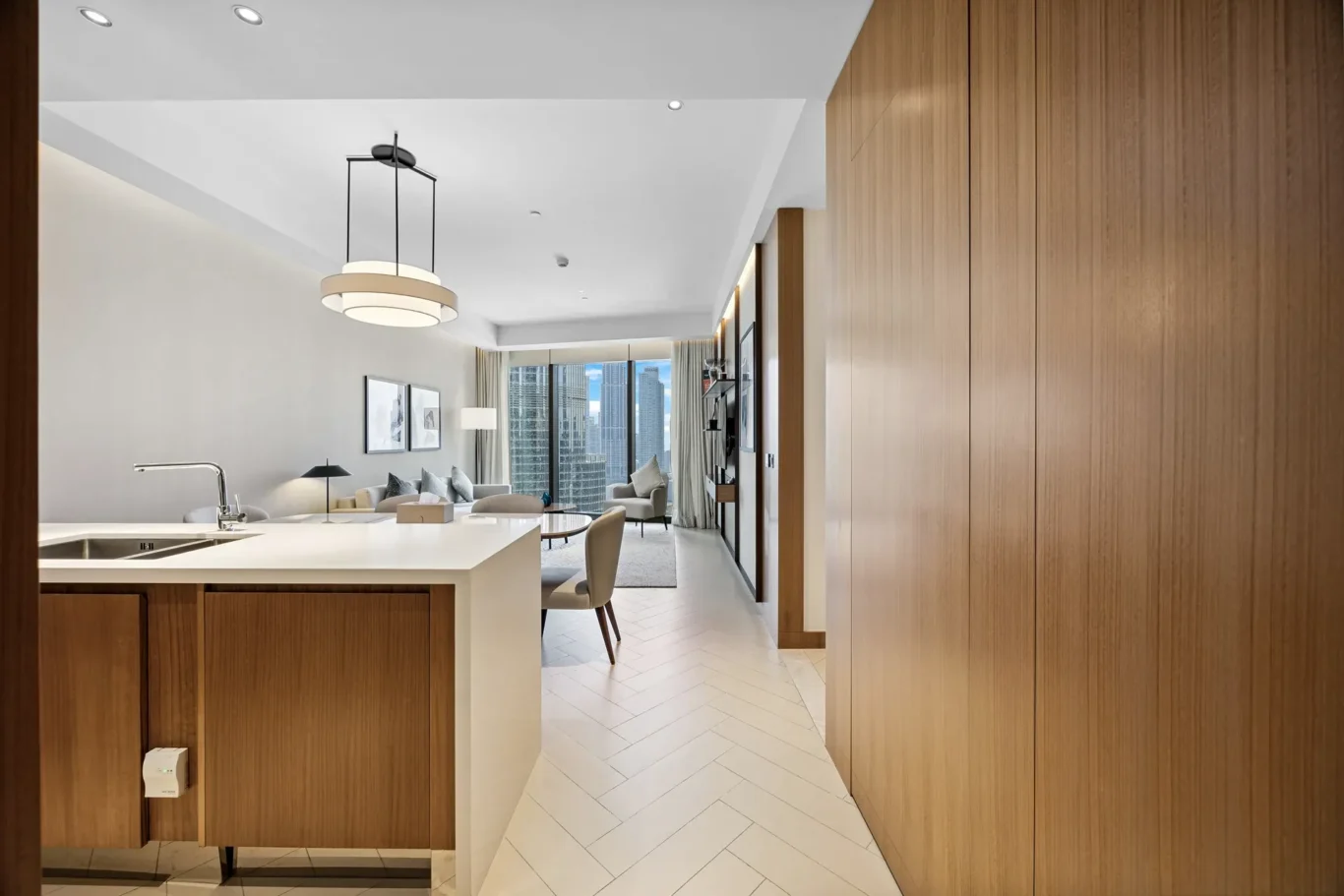 Modern open-plan kitchen and living area with a white island, wooden cabinets, and a city skyline seen through large windows.