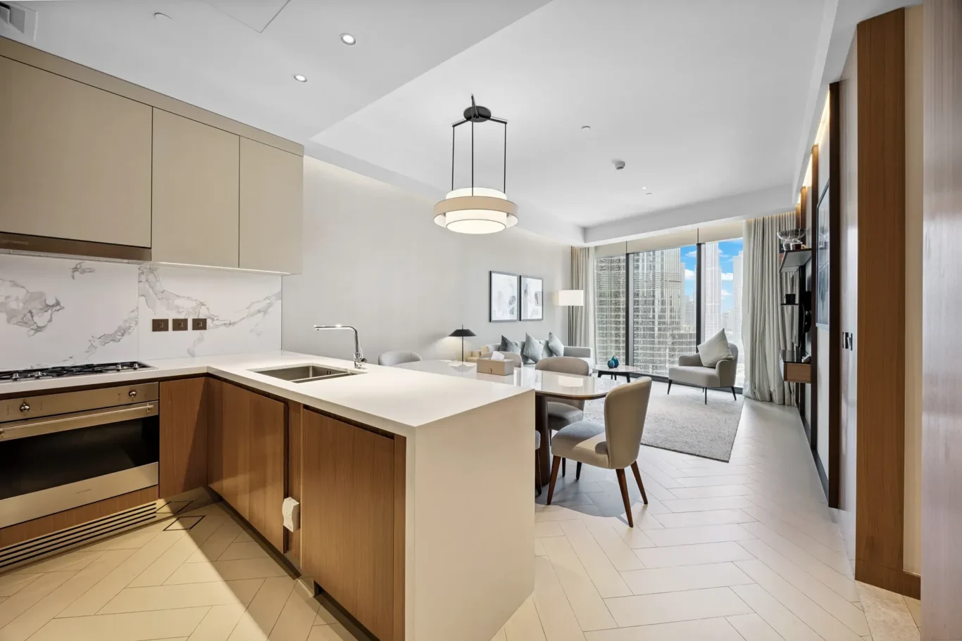 Open-concept kitchen with a white island, beige cabinets, and seating overlooking a living area with a city skyline through large windows.