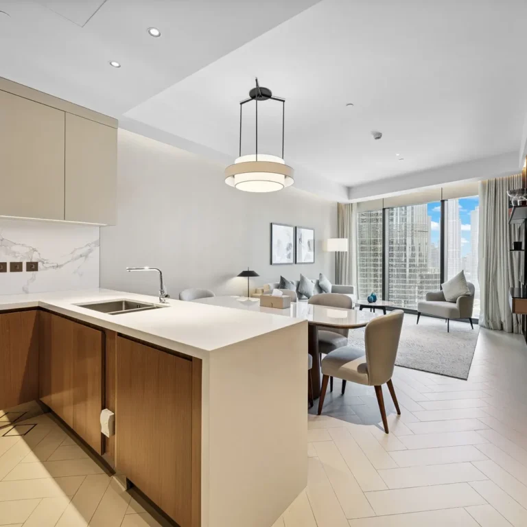 Open-concept kitchen with a white island, beige cabinets, and seating overlooking a living area with a city skyline through large windows.