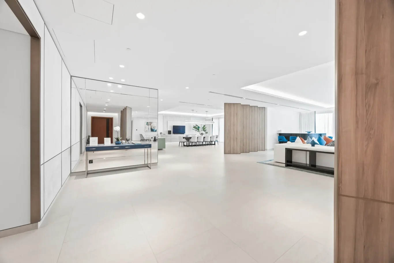 Bright modern showroom lobby with white walls, glass partitions, a reception desk on the left, and blue-cushioned seating area to the right.