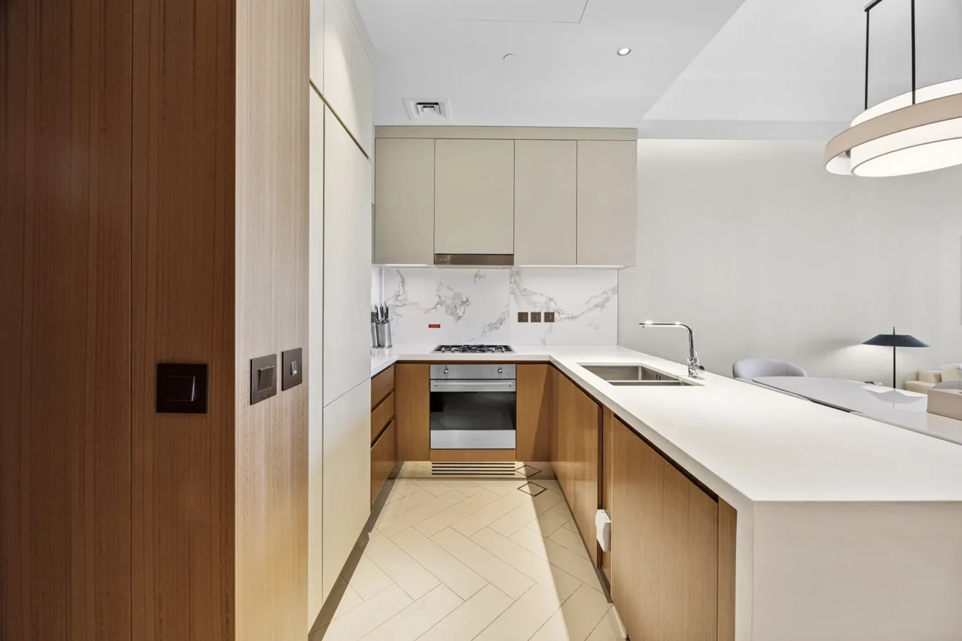 Modern kitchen with white countertops, beige upper cabinets, marble backsplash, and a wooden island along a slim galley layout.