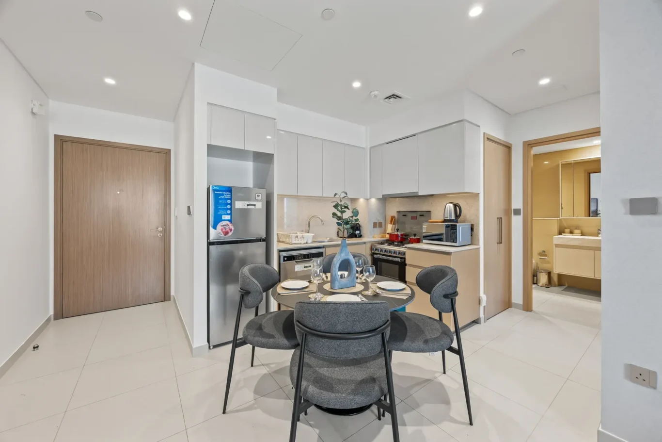 Open-plan kitchen with white cabinets, stainless steel fridge, and a round table set for four.