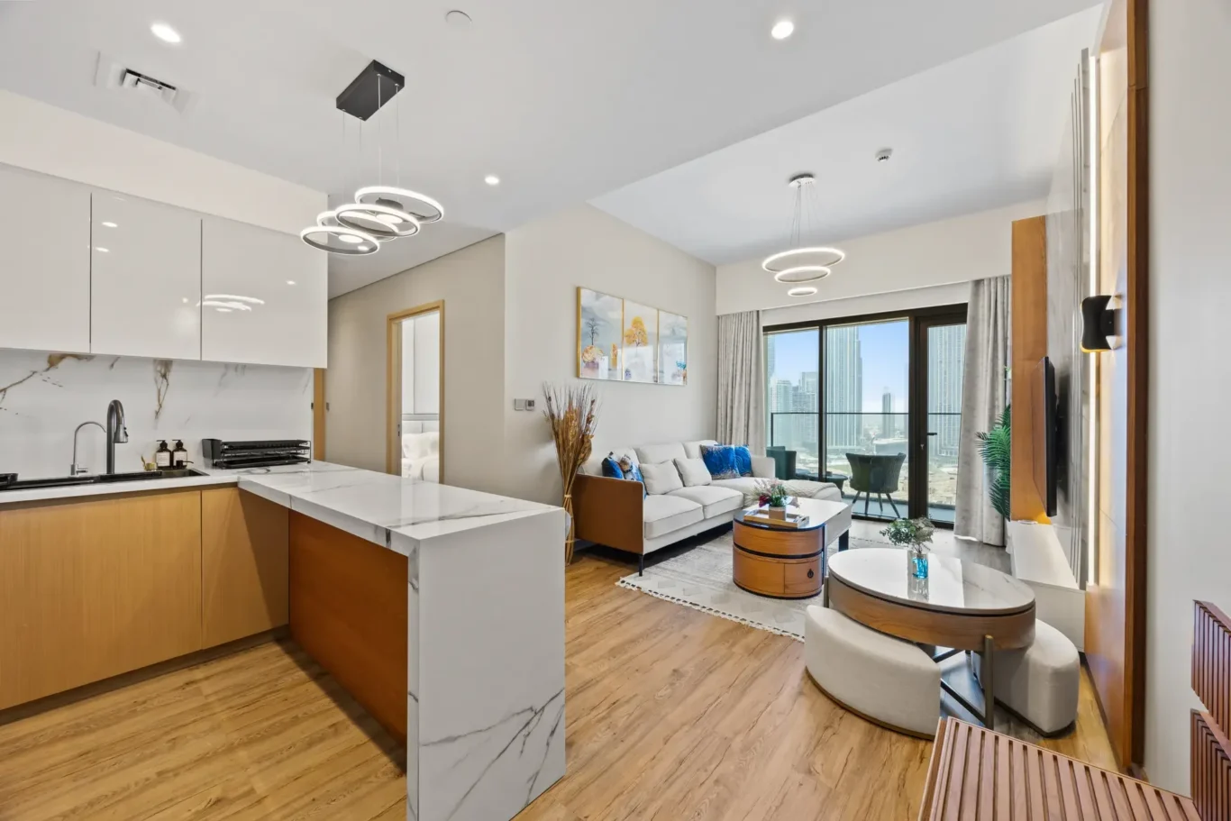 Open-plan living area with marble kitchen island, white cabinets, and looping pendant lights above.