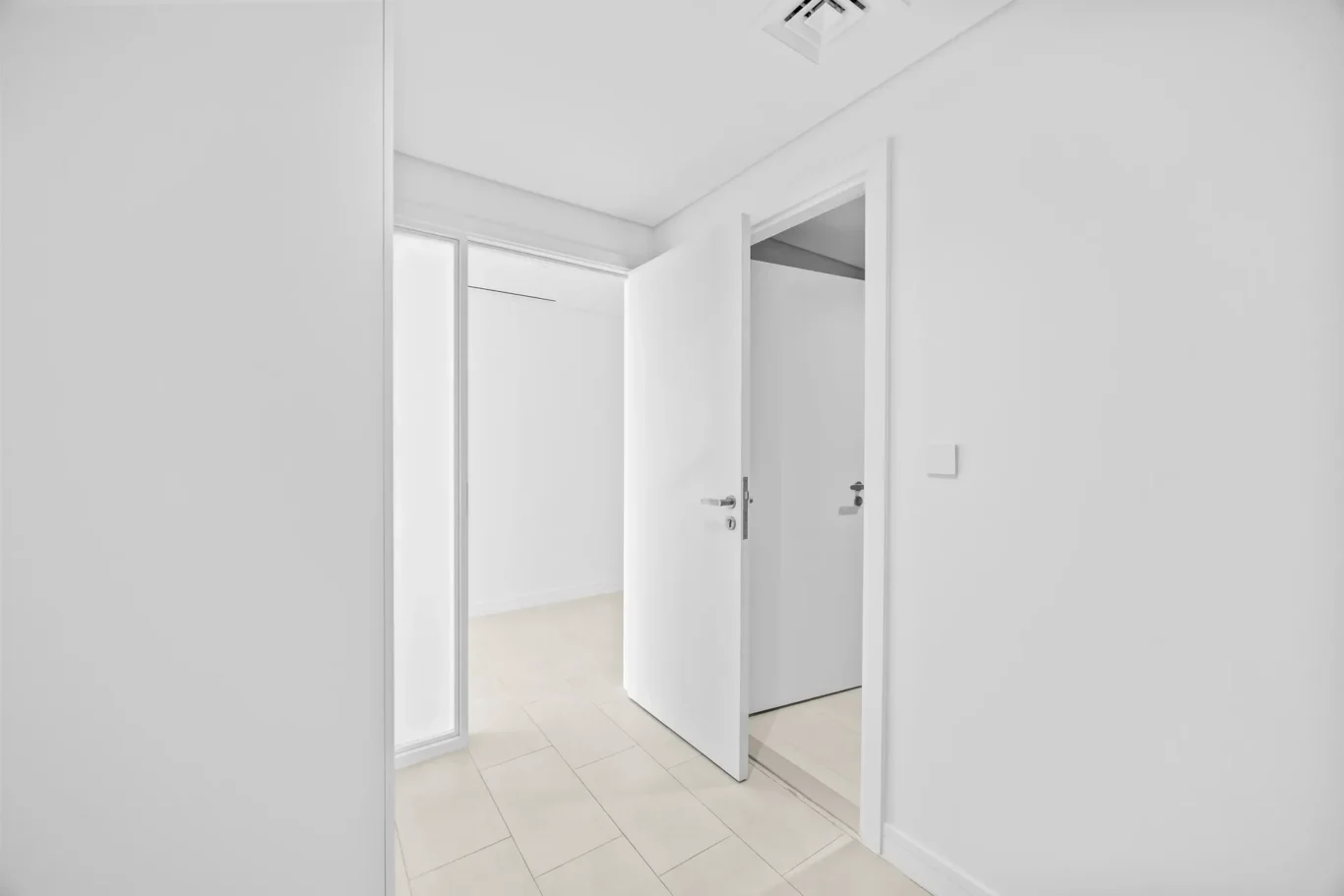 White hallway with open white doors leading into a bright room; light tiled floor visible at the threshold