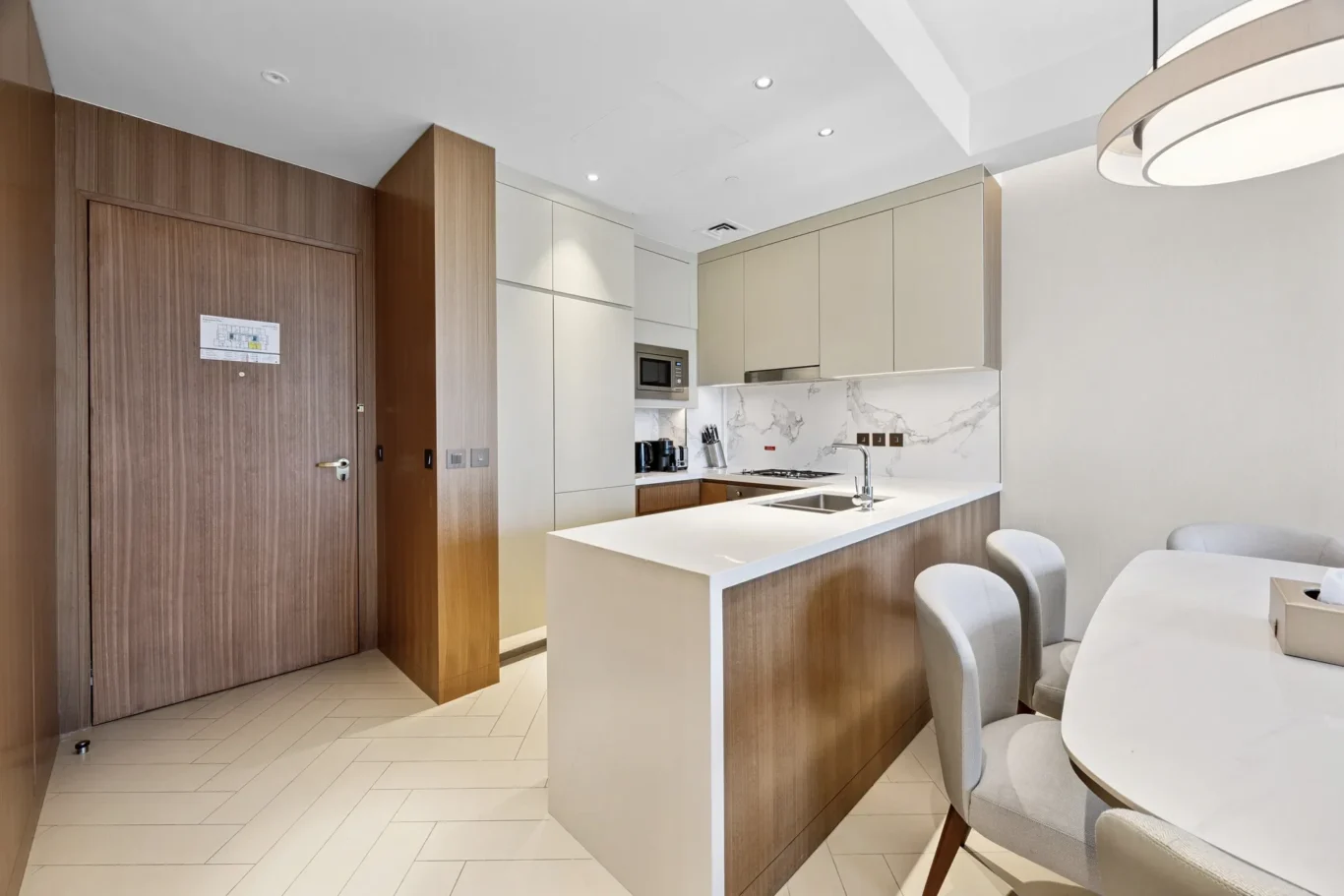 Modern kitchen with white cabinets, marble backsplash, and wood accents around an island and dining chairs.