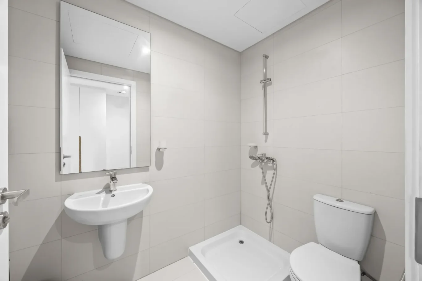 Modern white bathroom with a wall-mounted sink, large rectangular mirror, and a shower area with a handheld spray and chrome fixtures.