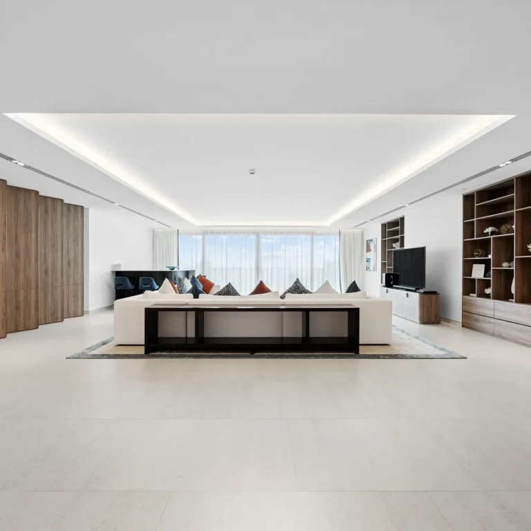 Spacious modern living room with a white sofa, wood-paneled cabinets, and open shelving along the wall.