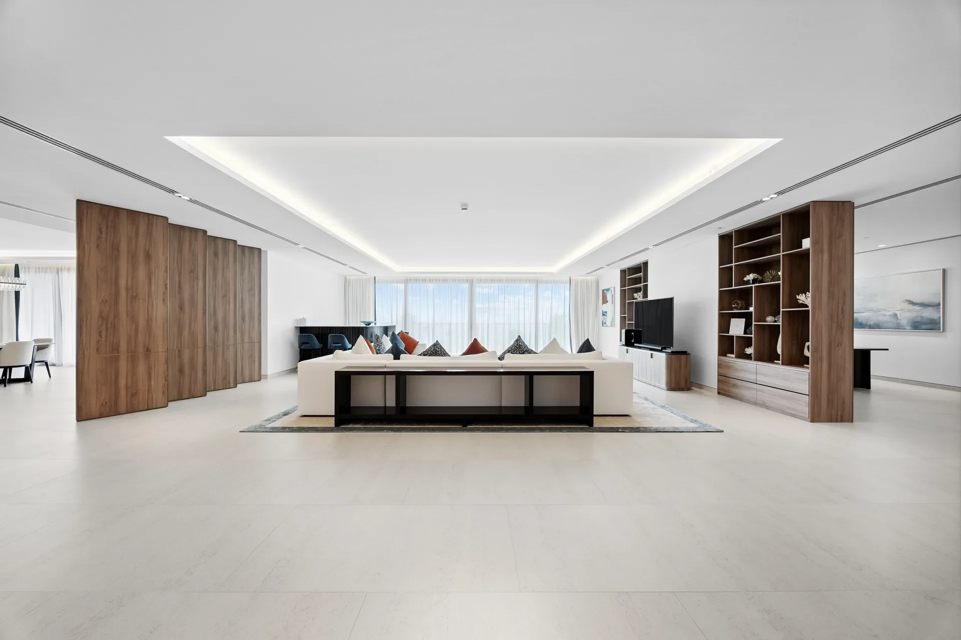 Spacious modern living room with a white sofa, wood-paneled cabinets, and open shelving along the wall.