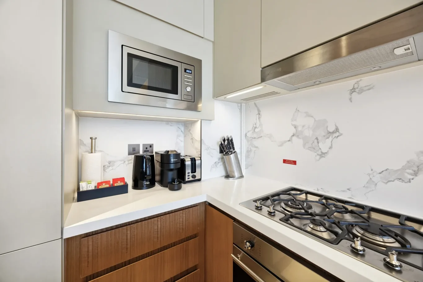 Modern kitchen counter with stainless microwave, coffee maker, toaster, knife block, and gas range against a marble backsplash.