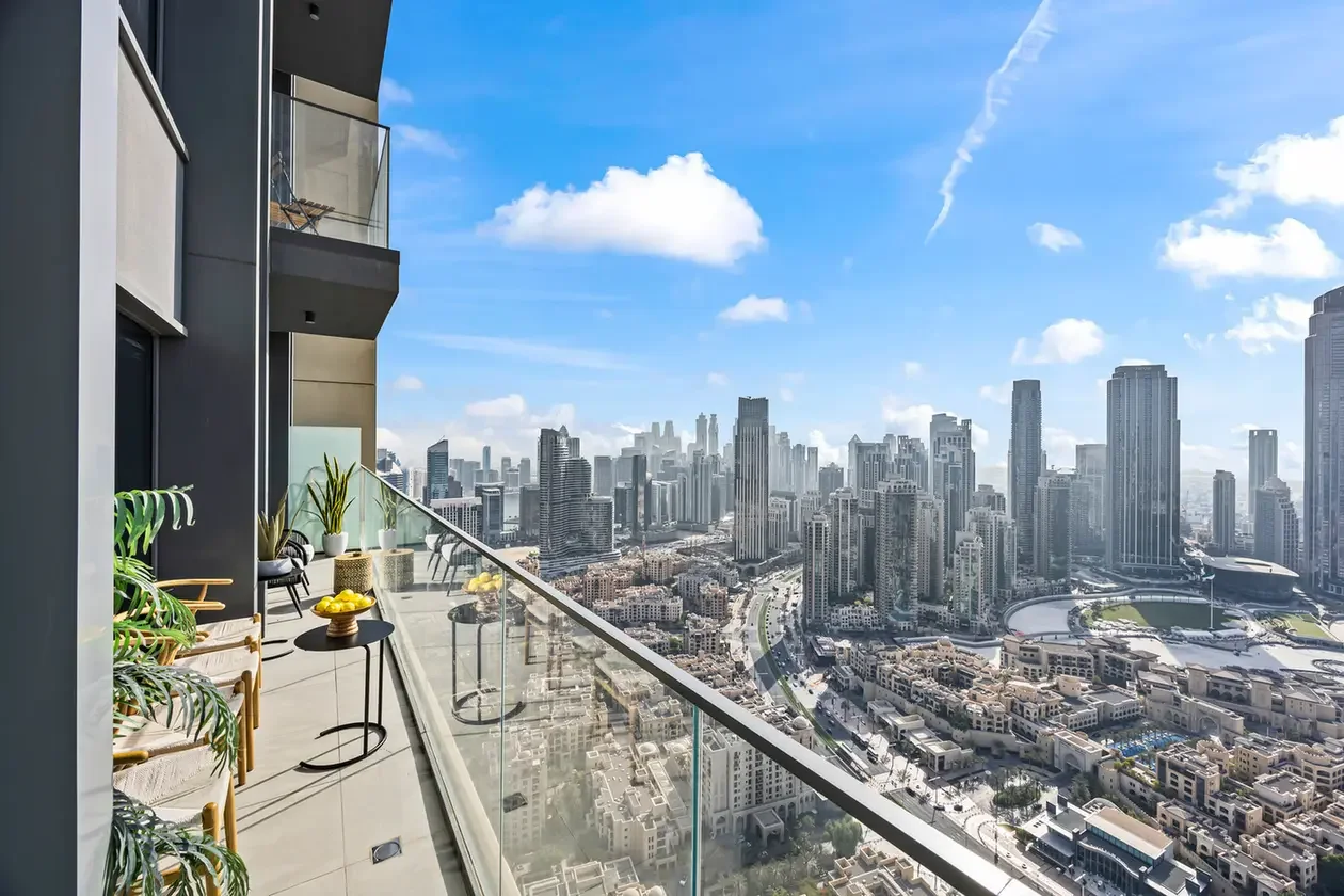 Balcony with glass railing and seating overlooking a dense city skyline of tall skyscrapers on a sunny day