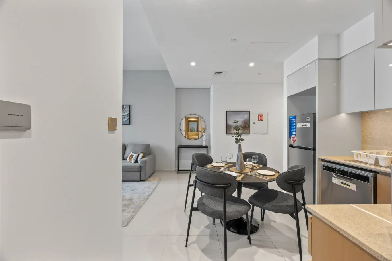 Round dining table with six gray chairs in a modern open-plan kitchen and living area.