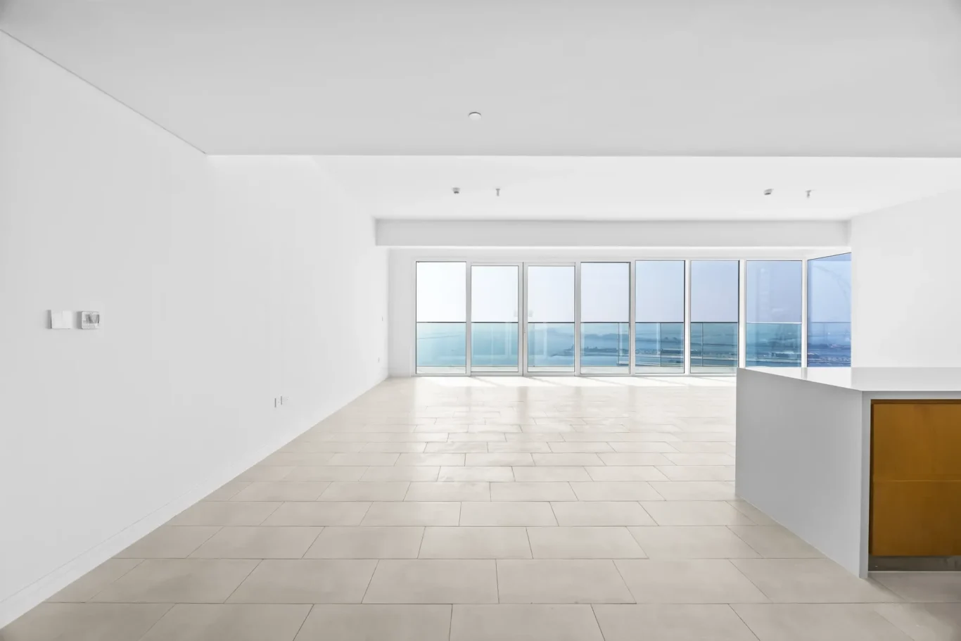 Bright empty living area with large glass doors to a balcony and ocean view.