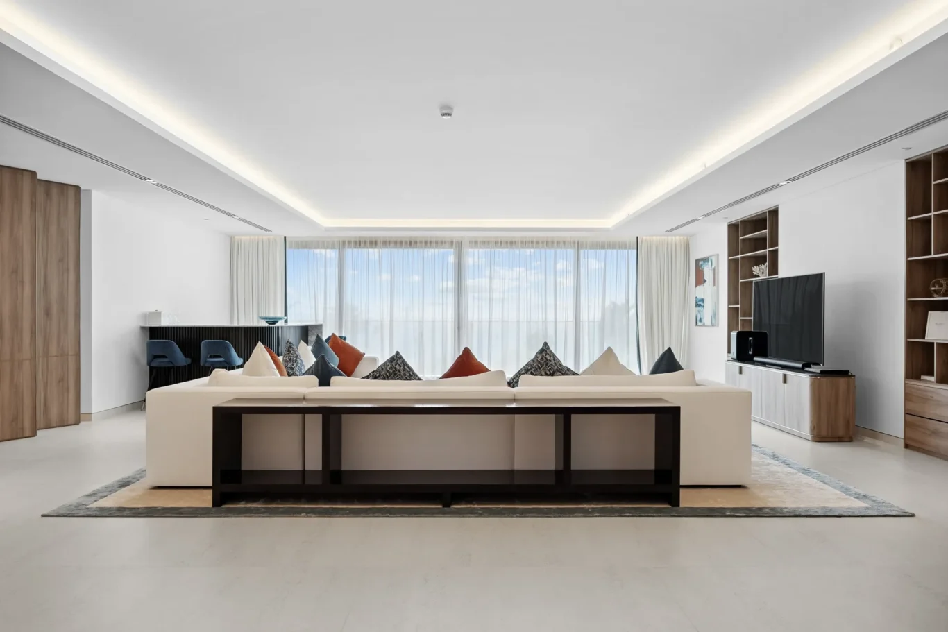 Bright open living room with a white sectional, colorful cushions, and a large window view with sheer curtains.