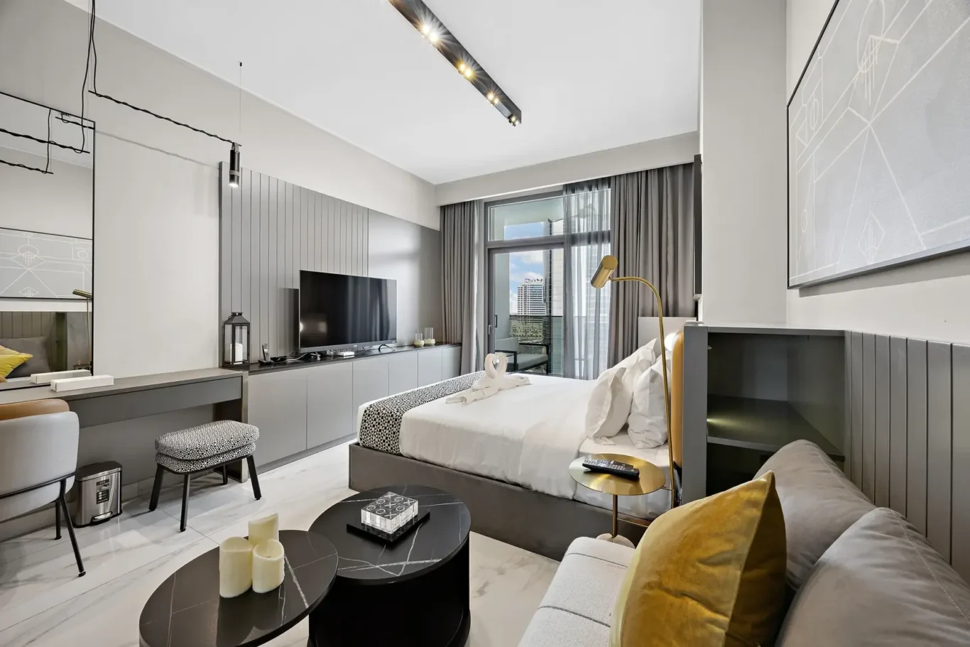 Modern hotel suite with a king bed, gray paneling, and a mounted flat-screen TV across from the bed.