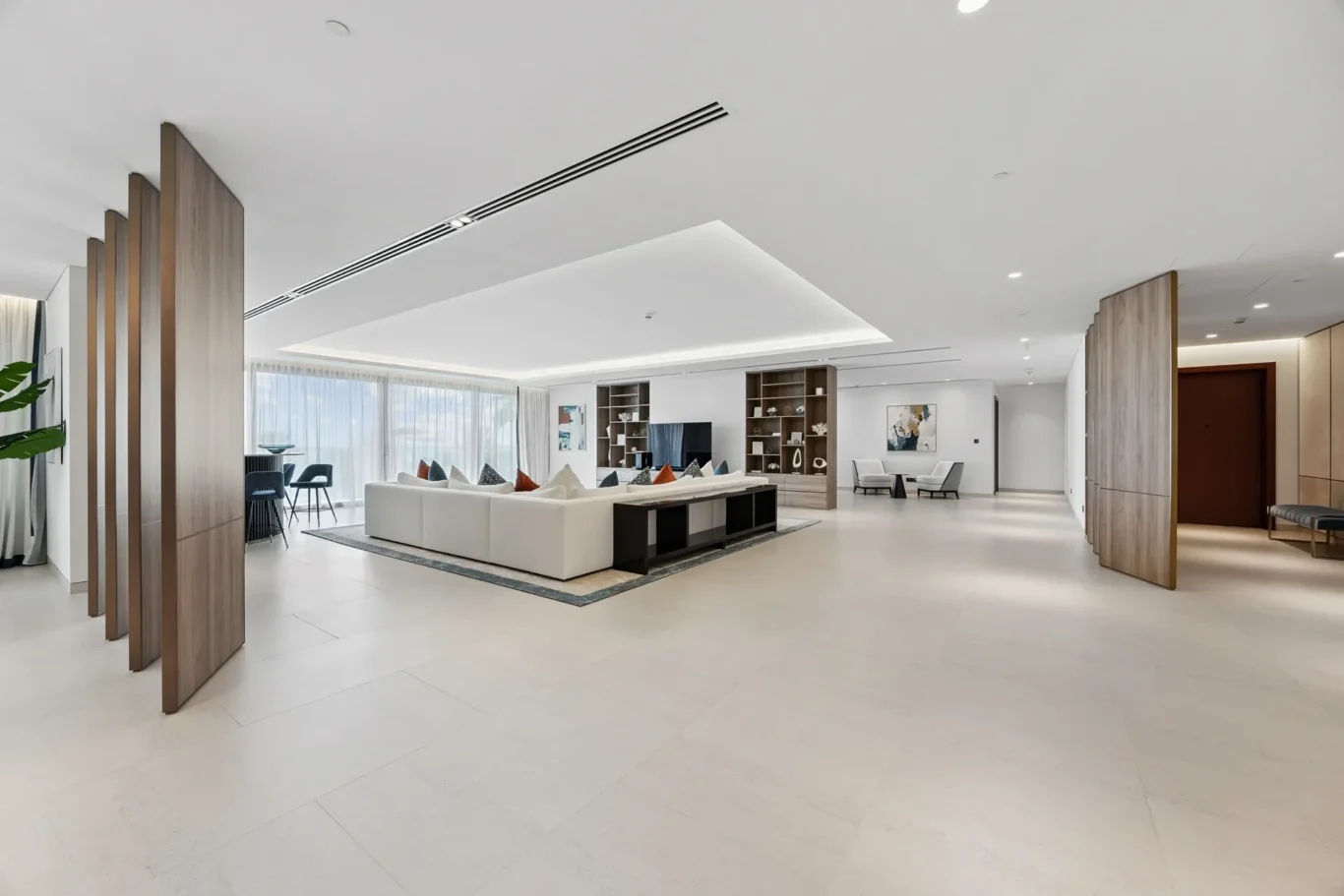 Spacious modern living room lobby with a white sectional sofa, wooden shelves, and large windows letting in natural light.