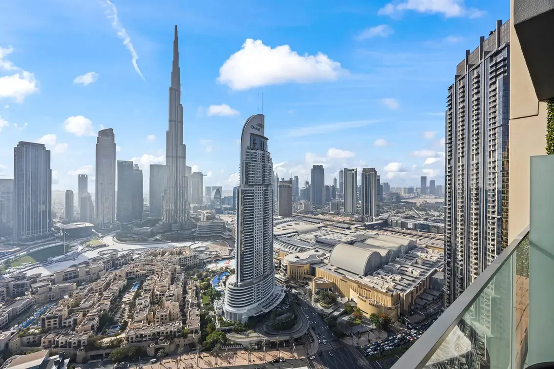Panoramic view of Dubai's skyline featuring the Burj Khalifa, taken from a balcony overlooking high-rise towers and a busy city block.
