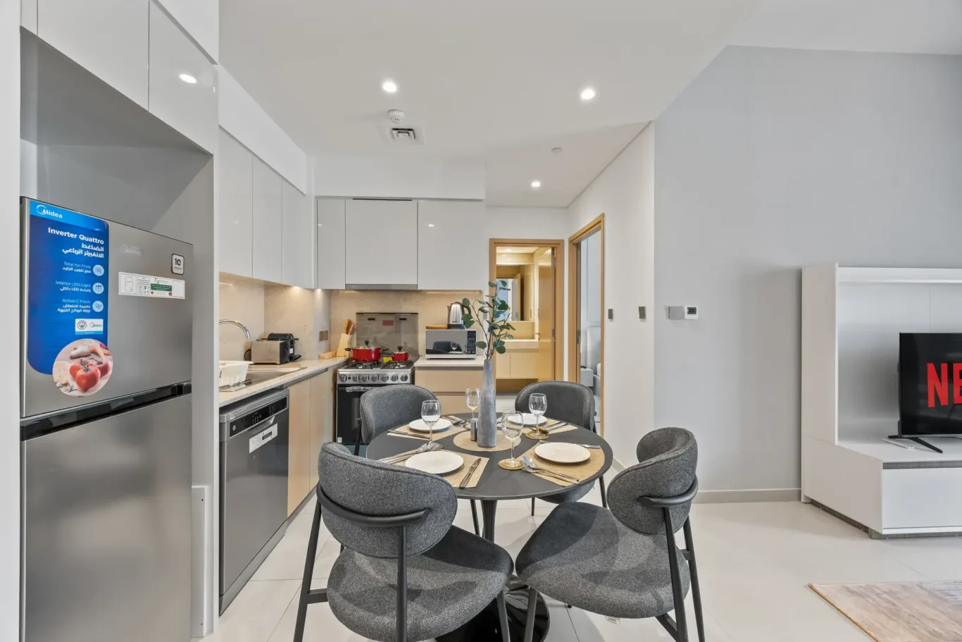 Modern open-plan kitchen with white cabinets, stainless appliances and a round dining table set for four.