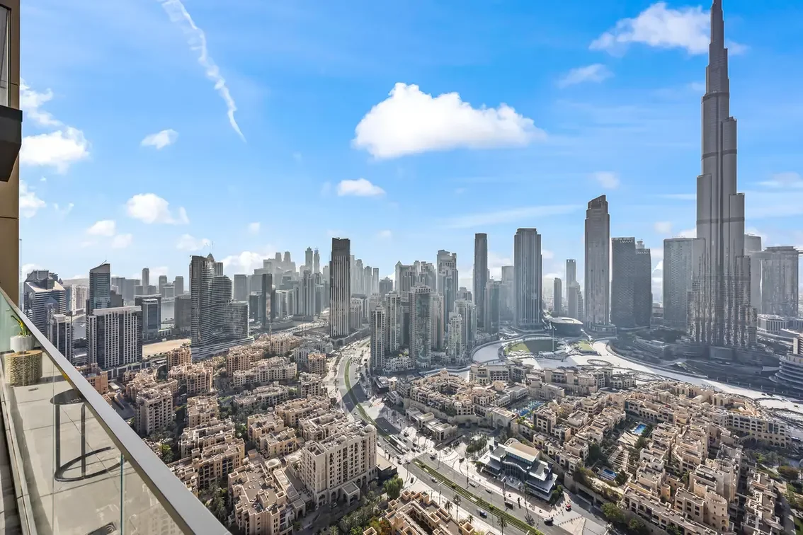 Panoramic cityscape with a dense mix of low-rise and high-rise buildings and a tall spire on the right beneath a blue sky.