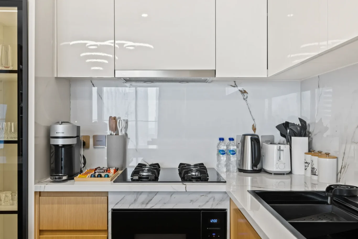 Modern white kitchen with a marble backsplash, stainless range hood, and a gas cooktop under ceiling cabinets.