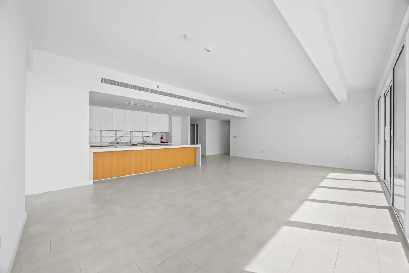 Bright open, modern kitchen area with white cabinets, an orange-fronted counter, and large glass doors on the right letting in daylight.