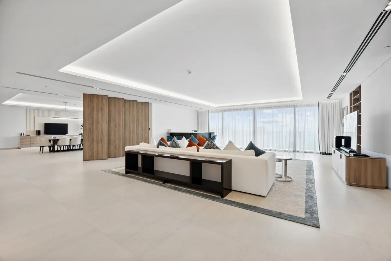 Spacious modern living room with a white sectional sofa, multicolored cushions, and a wooden room divider near a bright dining area.