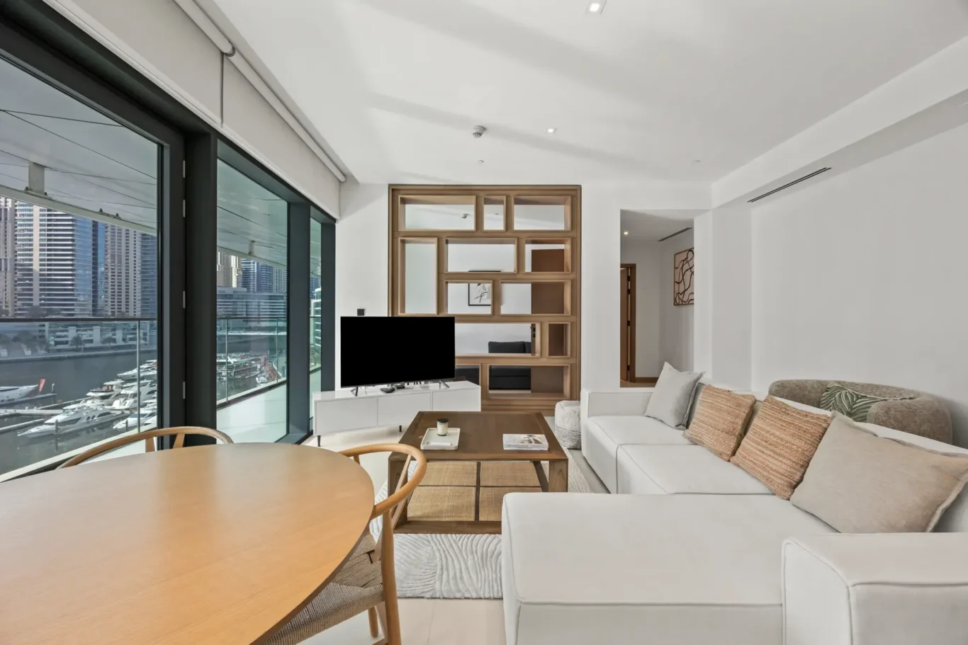 Spacious living room with floor-to-ceiling marina views, white walls, and a wooden room divider.