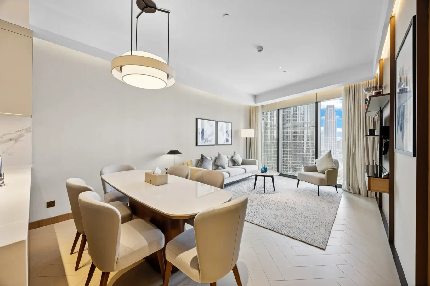 Open-plan living and dining area in a modern apartment with neutral furniture and a city skyline view through large windows.