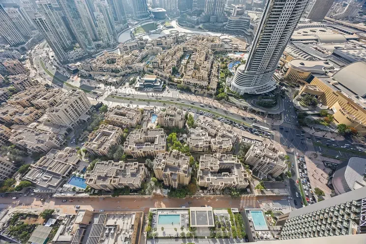 Aerial view of a dense urban area with low-rise beige residential blocks clustered together, surrounded by tall skyscrapers in a modern cityscape.