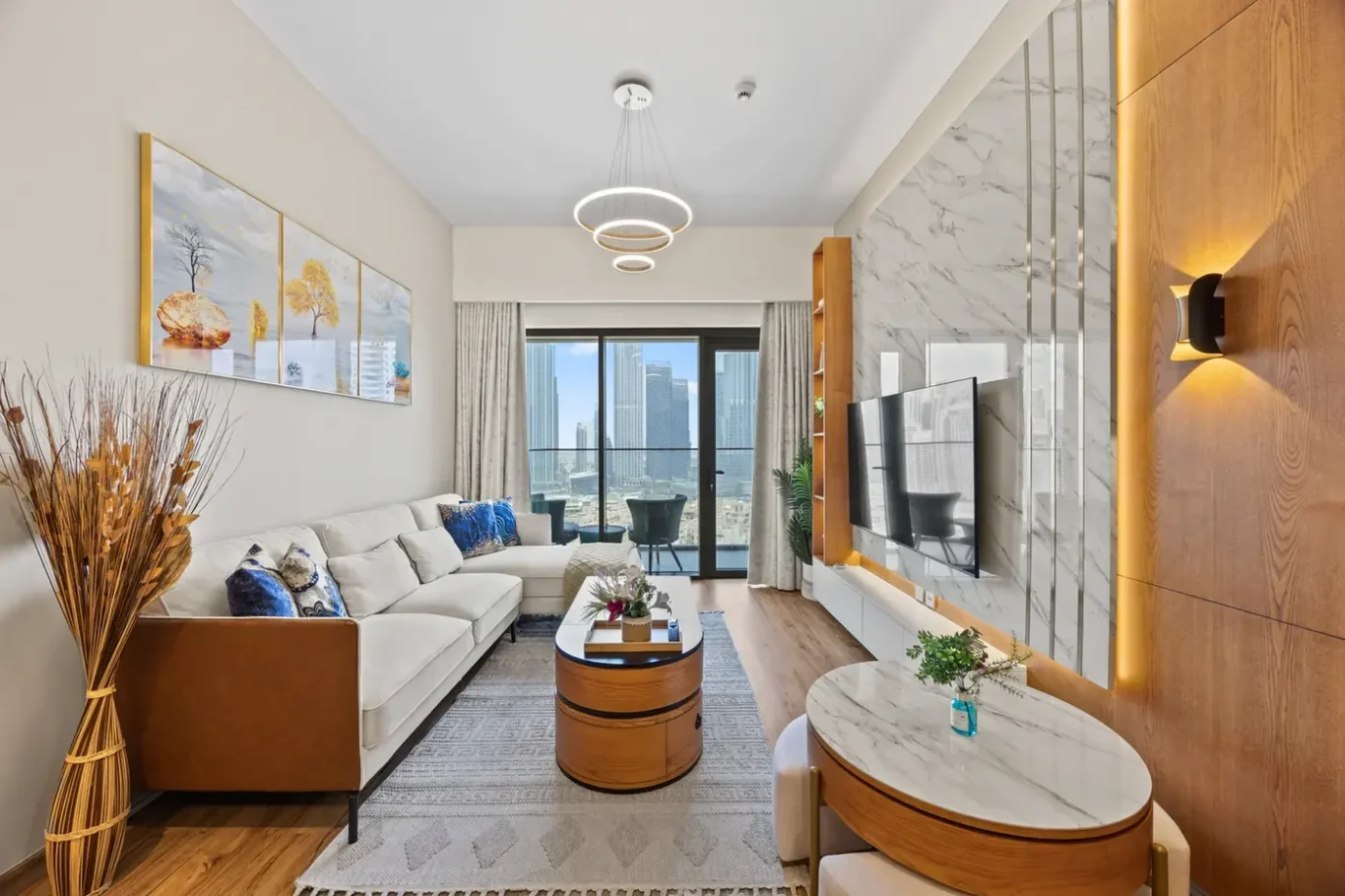 Modern living room with a white sectional sofa, neutral decor, and a balcony overlooking a city skyline.