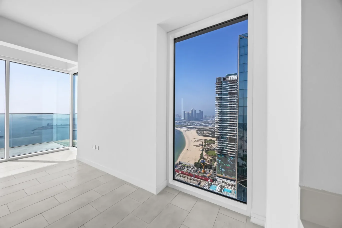 Bright living space with a large floor-to-ceiling window showing the beach and city skyline outside.
