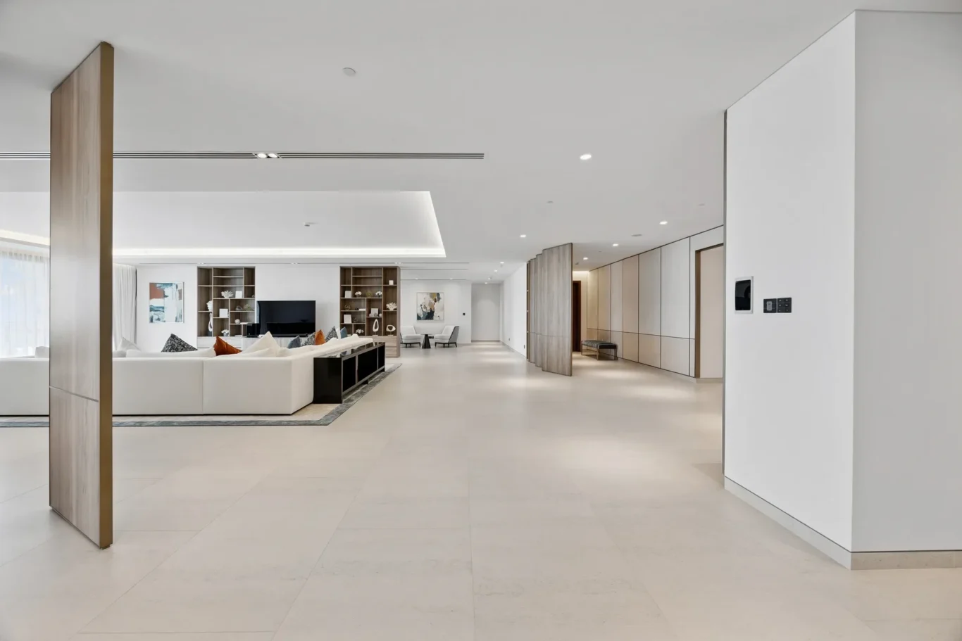 Open-concept living room with a white sectional sofa, built-in shelves, and a TV against a bright, minimalist backdrop.
