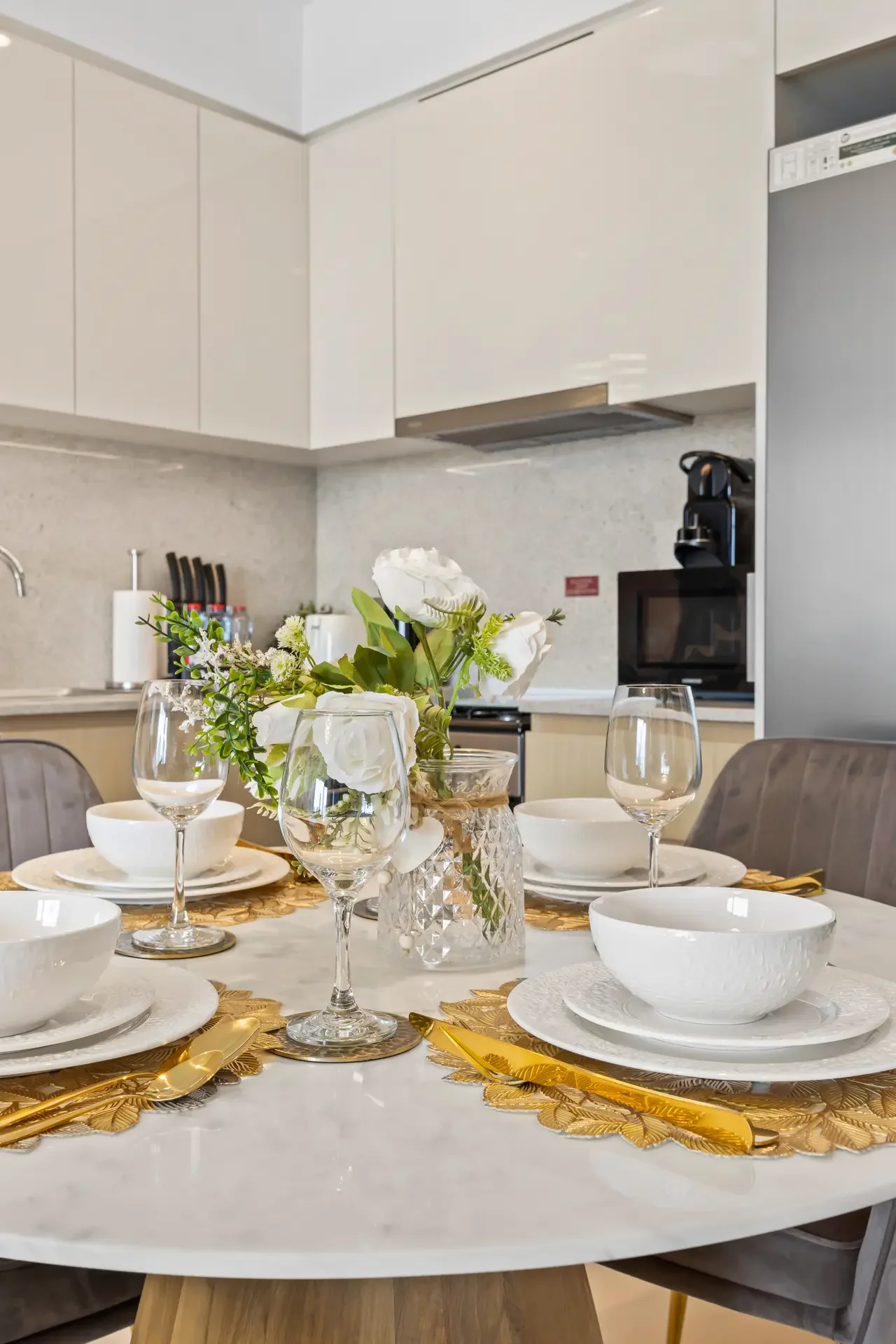 Elegant dining table set with white dishes, crystal glasses, and a floral centerpiece in a crystal vase, in a modern kitchen.