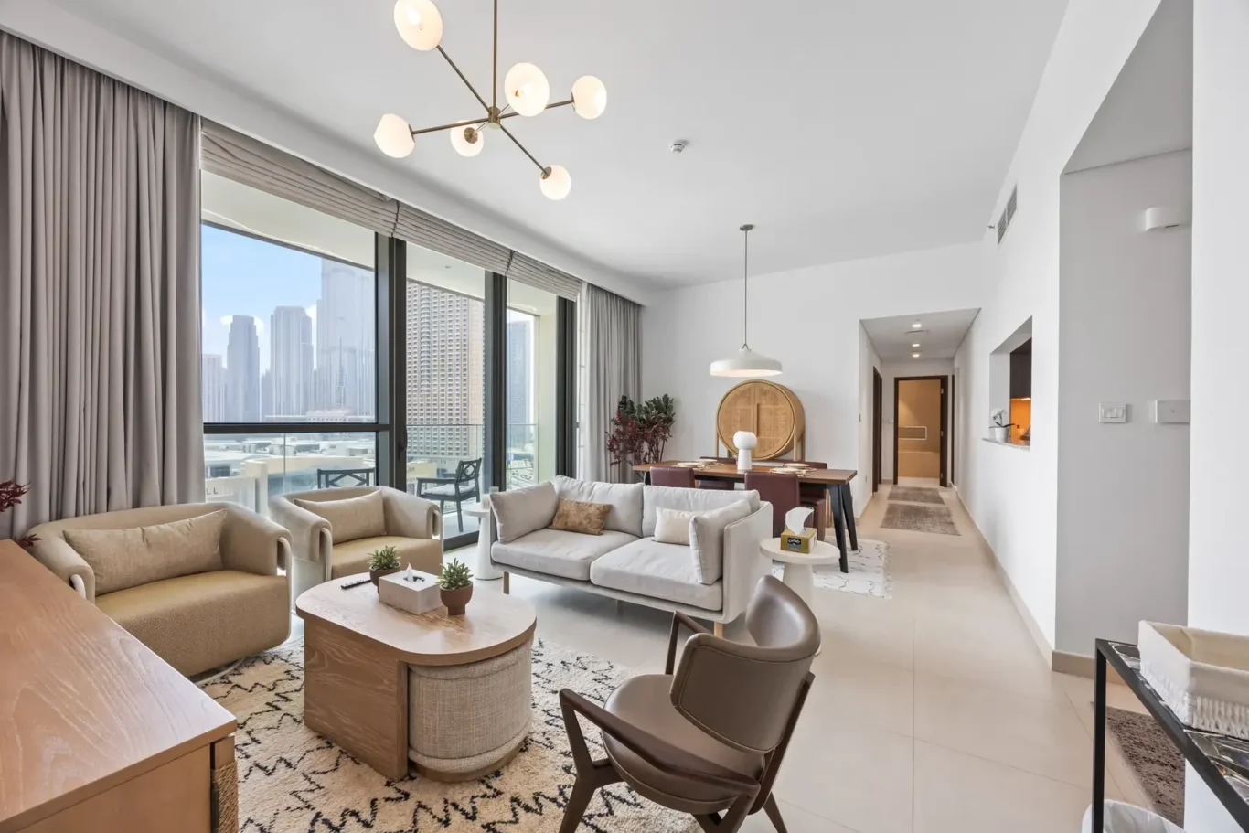 Bright open-plan living room with cream furniture and a city skyline view through floor-to-ceiling windows on the left.