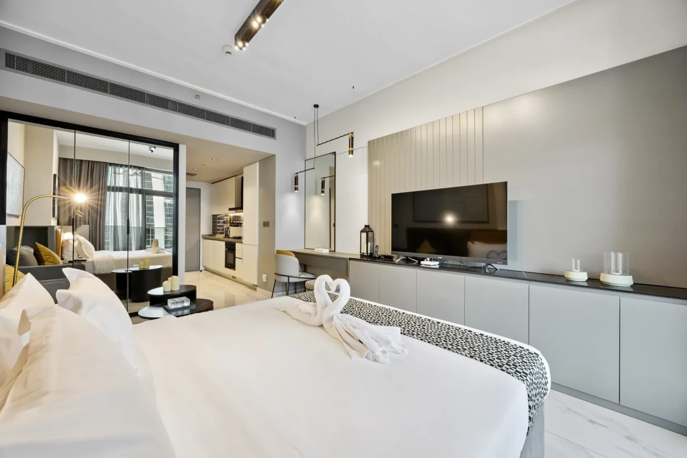 Modern hotel suite with a king bed, living area, and kitchenette in neutral gray tones.