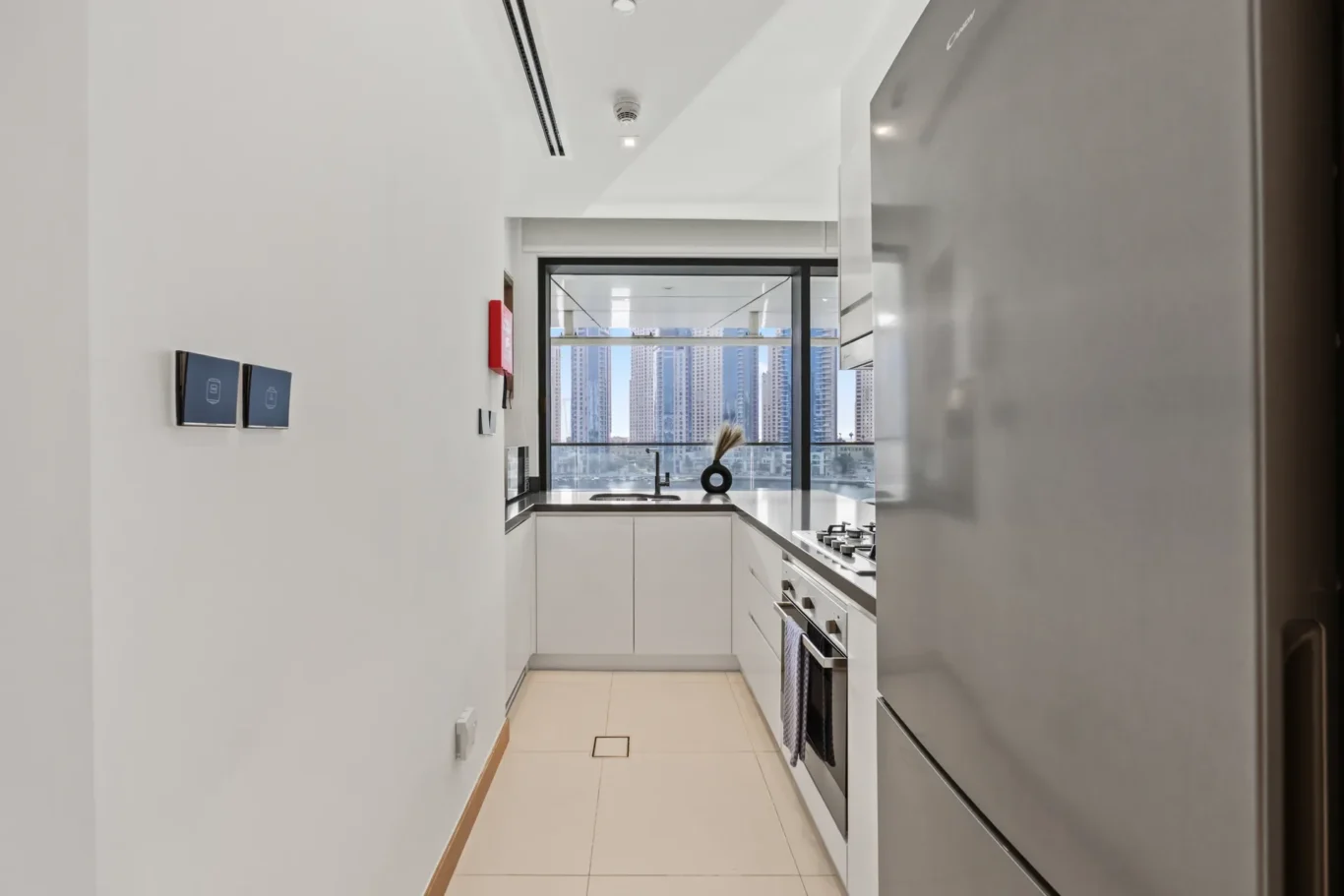 Modern galley kitchen with white cabinets, stainless steel appliances, and a cityscape view through a large window at the end of the room.