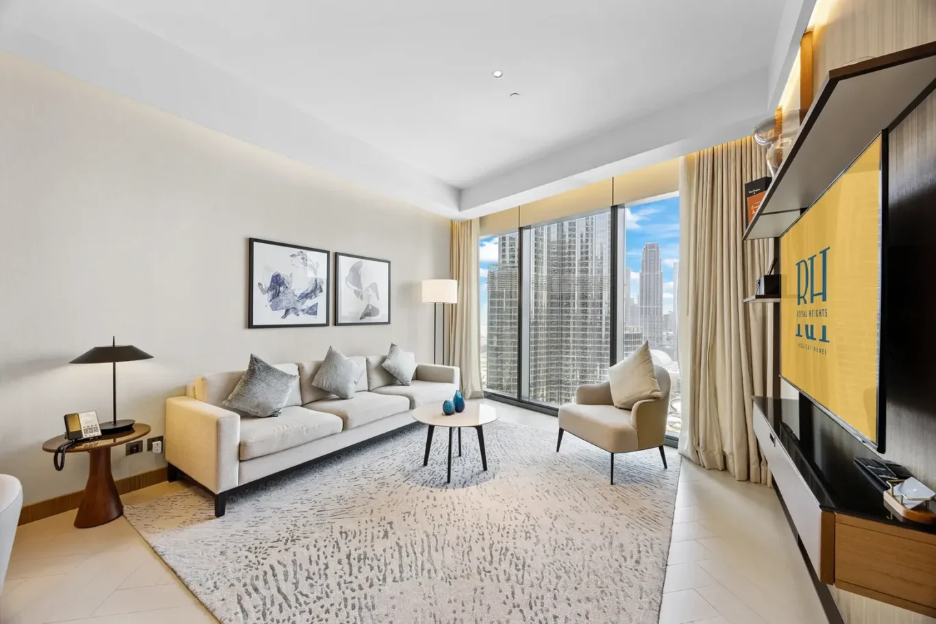 Bright hotel living area with beige sofa and armchair, coffee table, and a city skyline view through large windows.