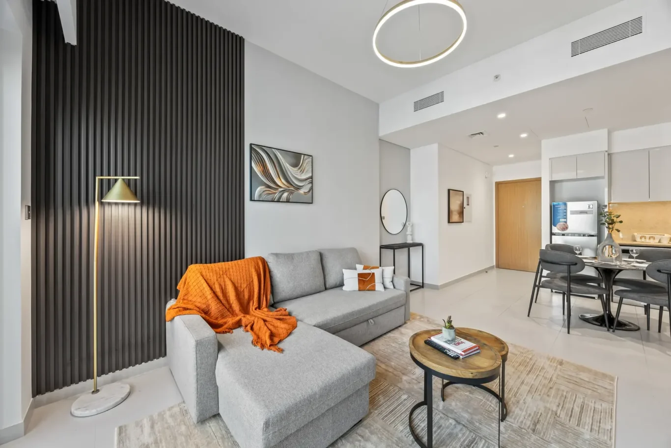 Open-plan living room with gray sofa, orange throw, black vertical accent wall, and round coffee tables beside a rug.