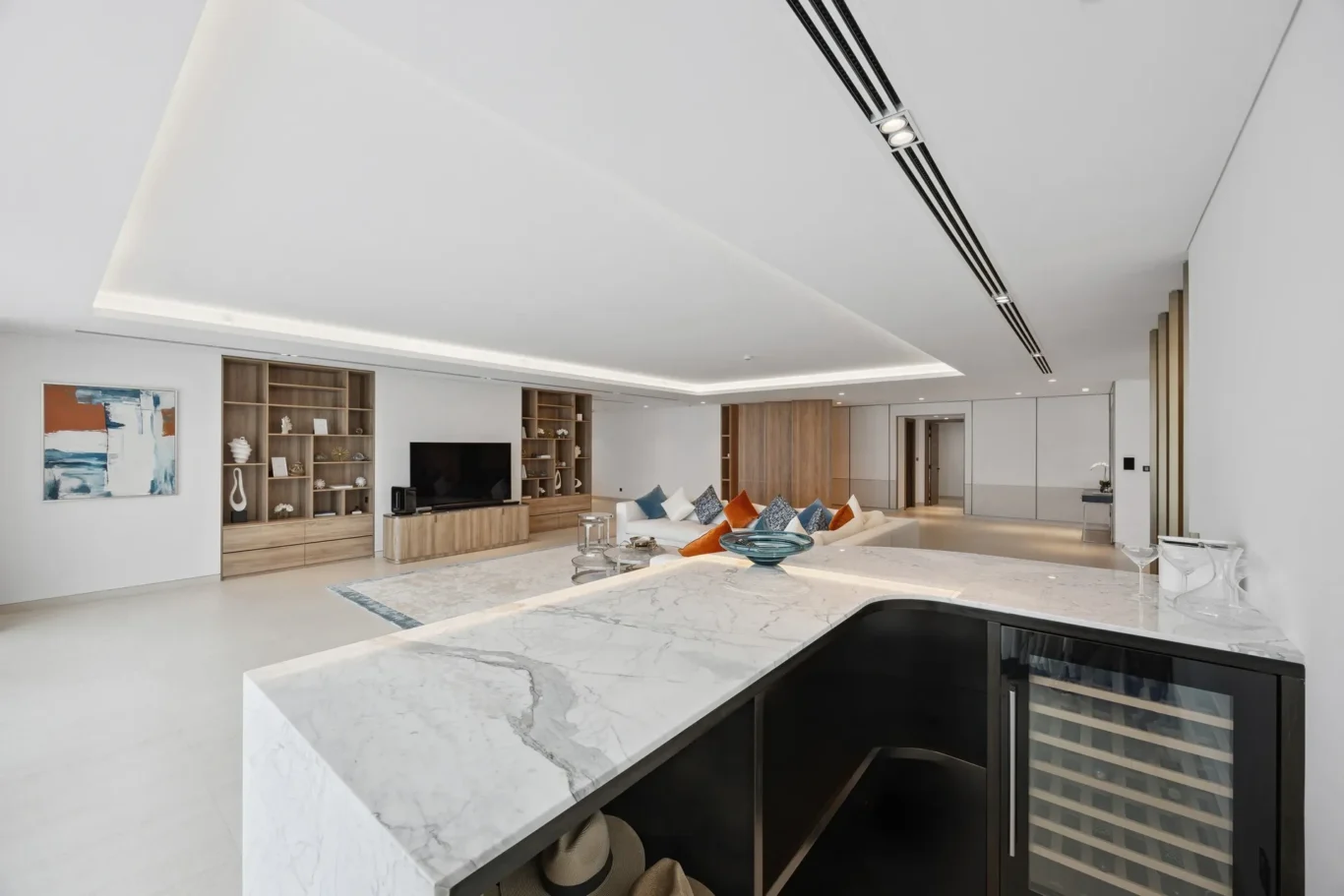 Open-concept living room with a marble kitchen island in the foreground, wooden shelving, and a large flat-screen TV