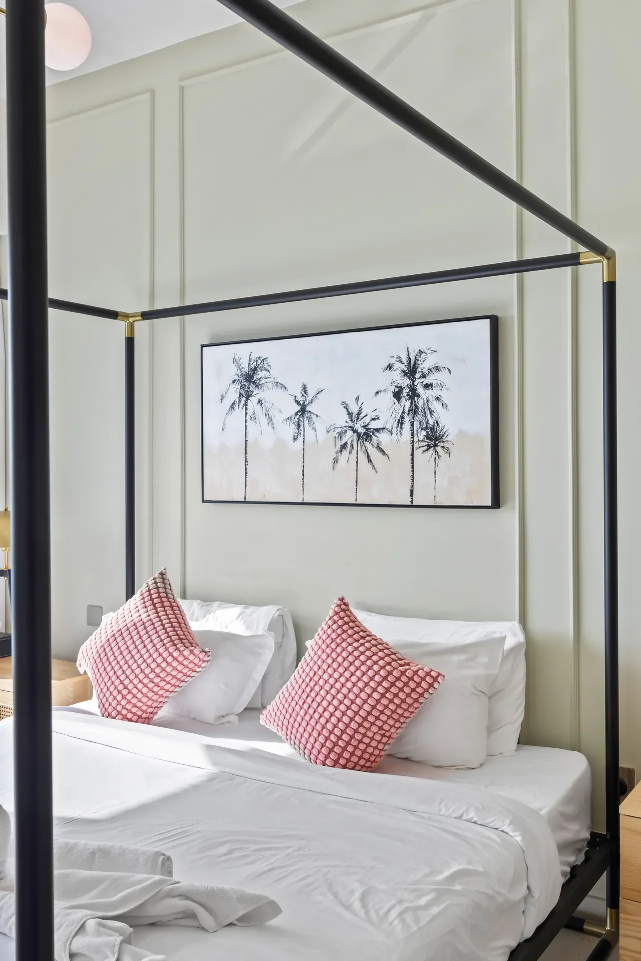 Metal canopy bed with black frame and brass accents, pale green paneled walls, and a palm tree artwork above the headboard.