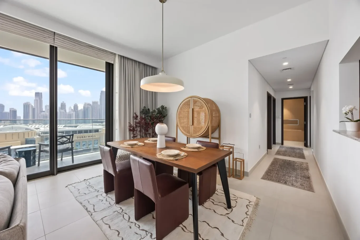 Modern dining room with a wooden table and six brown seats, overlooking the city skyline through large glass doors.