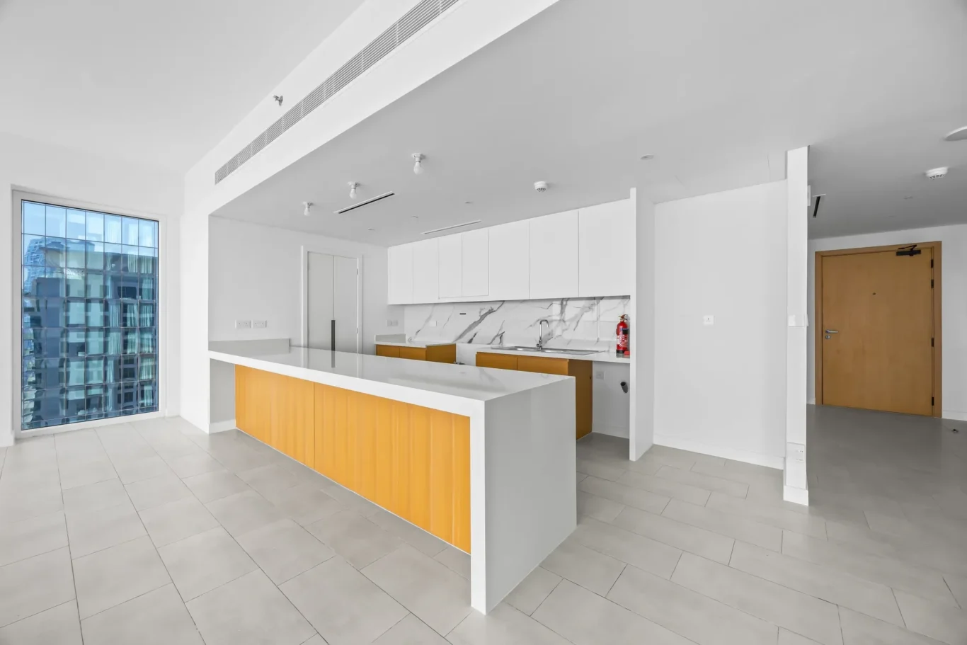 Bright white kitchen with marble backsplash, orange-accented island, and a large window overlooking a cityscape.