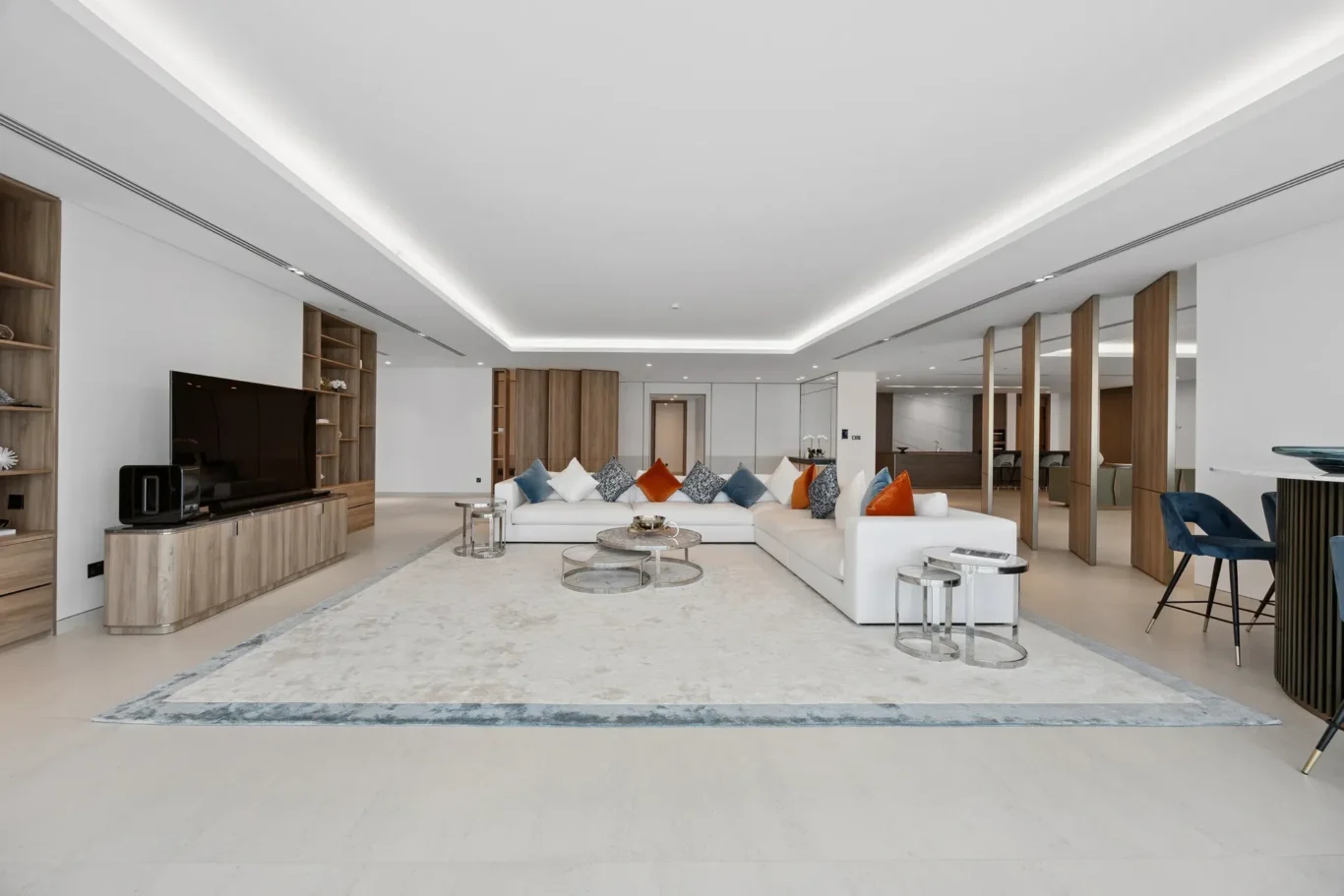Spacious modern living room with a white sectional sofa, colorful throw pillows, glass coffee tables, and a large area rug.