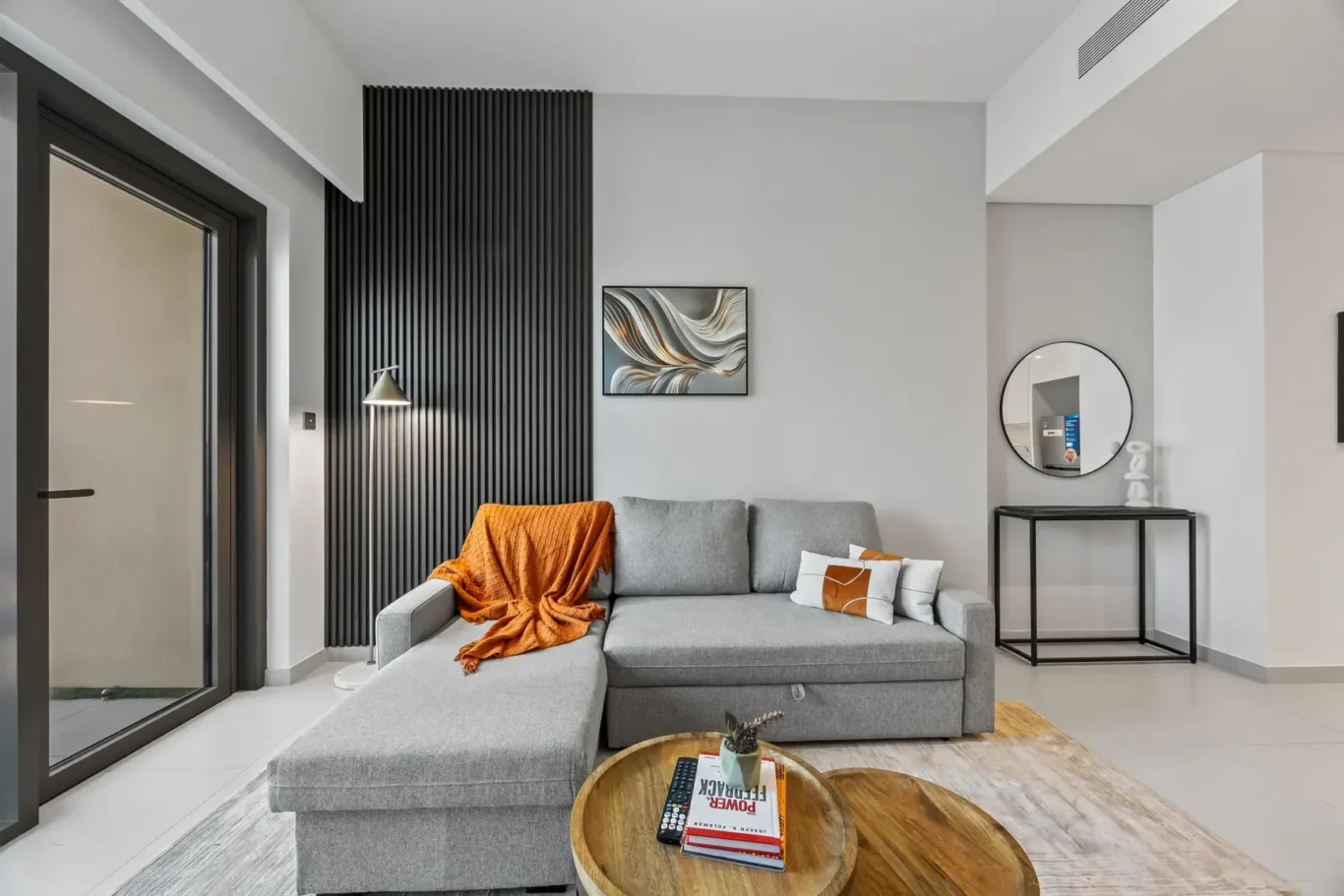 Modern living room with a grey sectional sofa, orange throw, and a black vertical-slat accent wall under soft lighting.
