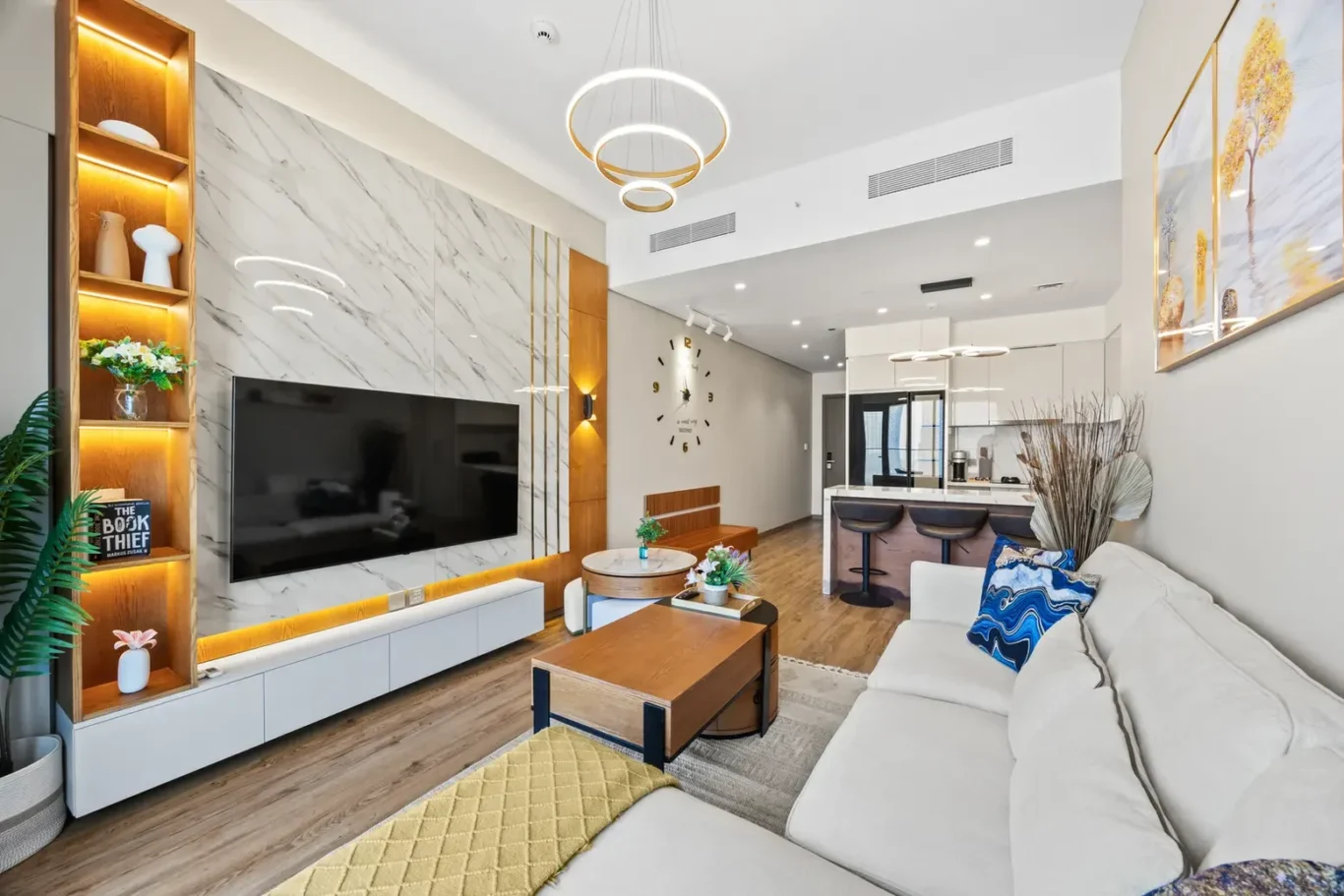 Modern living room with a large TV wall, marble panels, and warm wood accents; a white sofa and coffee table arrangement.