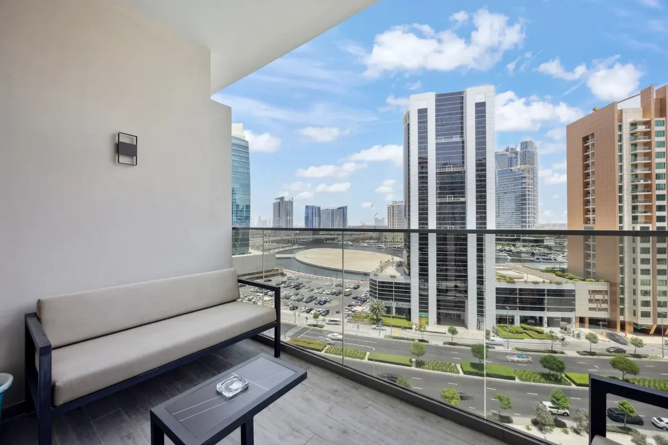 Balcony seating area with beige cushions overlooking a city skyline of tall glass buildings.