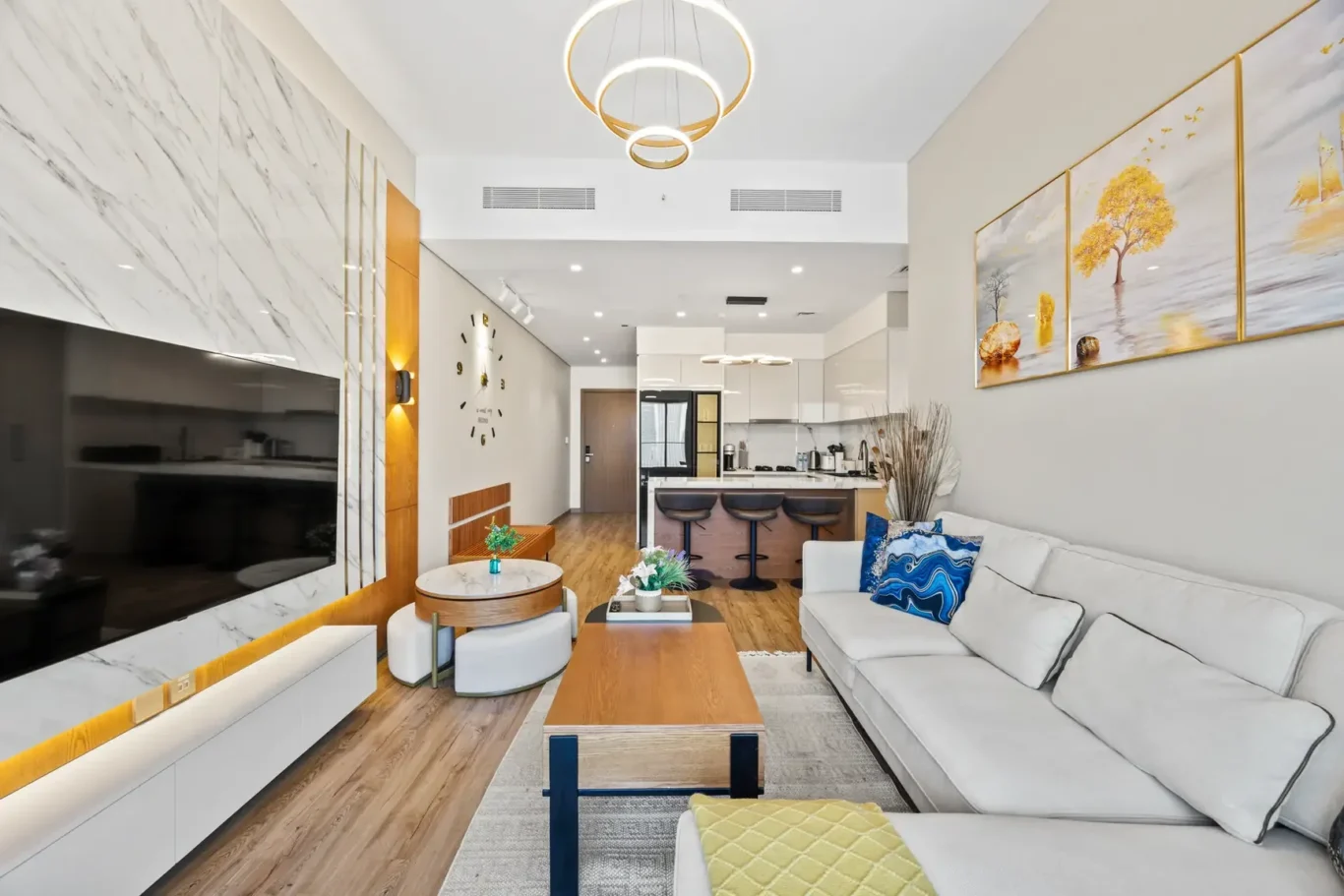Open-concept living room with a white sectional, wooden coffee table, and a view into the bright kitchen area.