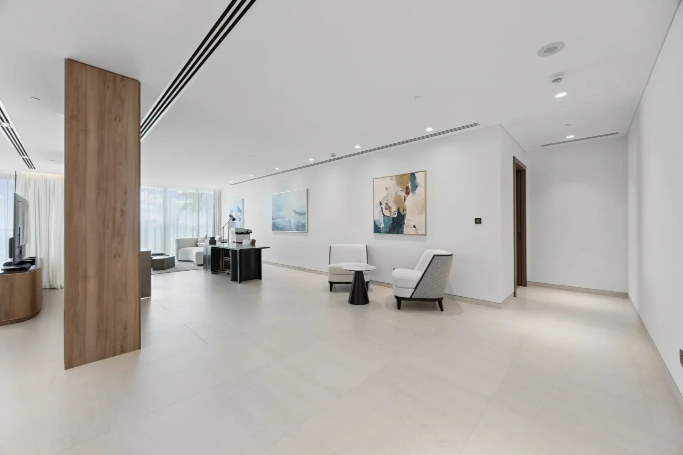 Open, bright modern office lobby with white walls, a large wooden pillar, and white lounge chairs beneath abstract wall art