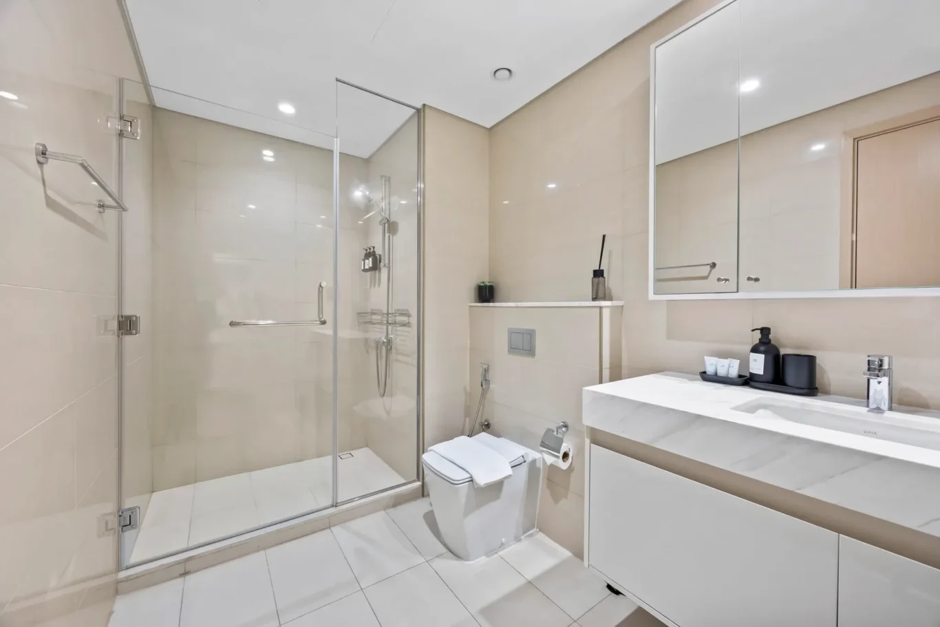 Contemporary bathroom with glass shower enclosure, wall-mounted toilet, and white marble vanity beneath a large mirrored cabinet.