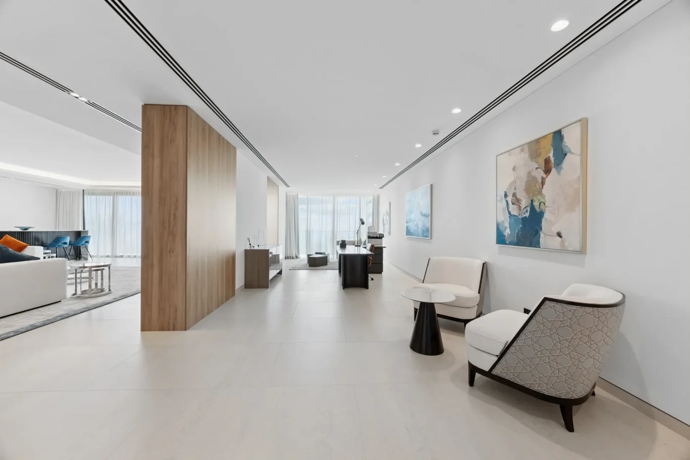 Spacious modern hotel lobby with white walls, a wooden column, and abstract wall art along a bright, open space.