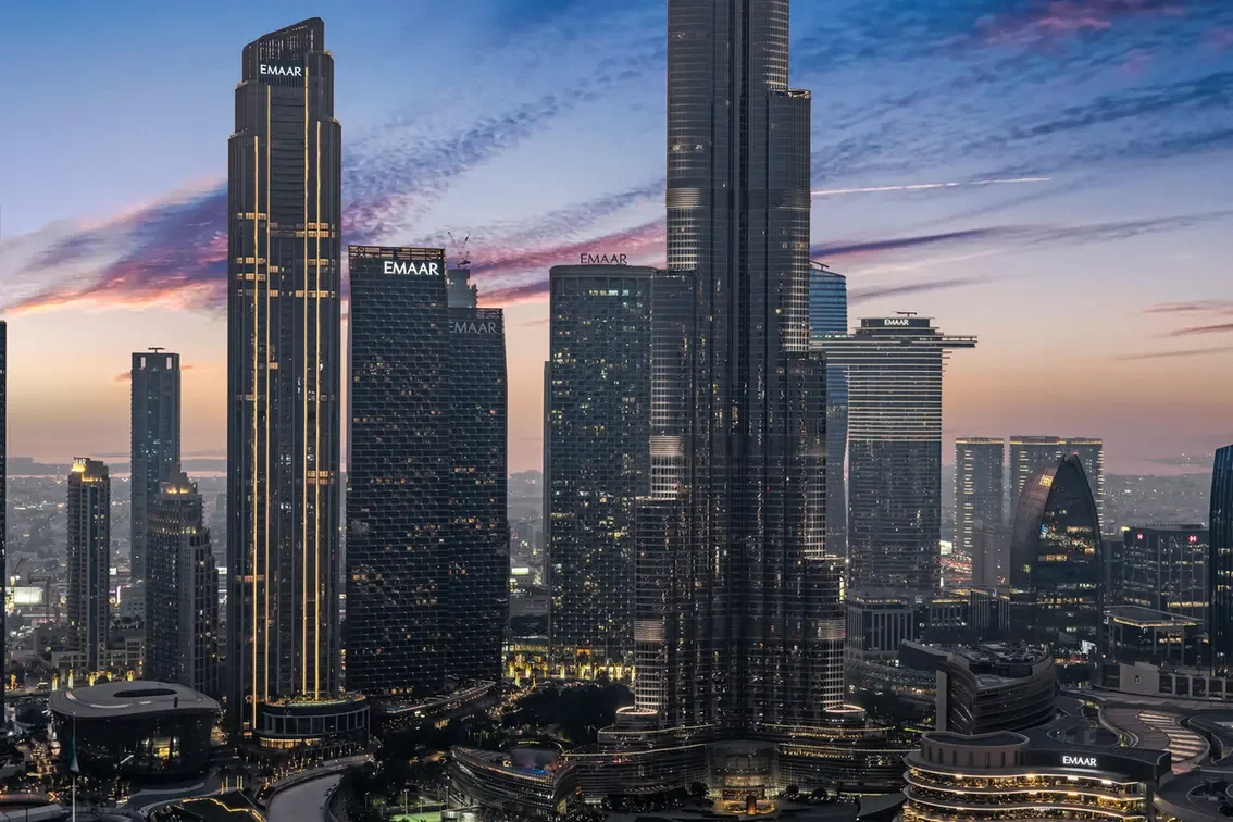 Dubai skyline at dusk featuring towering EMAAR skyscrapers and a purple-orange sunset sky
